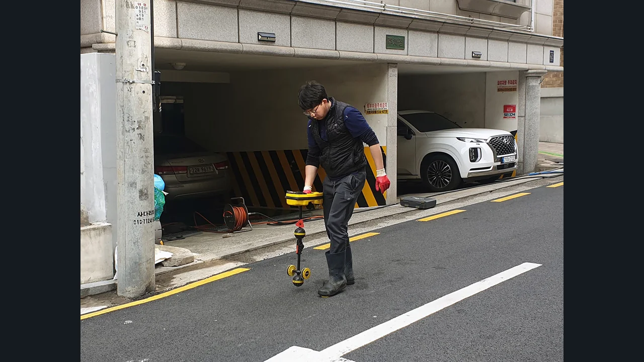 건물 주차장 입구에서 지면에 탐지기를 대는 작업자